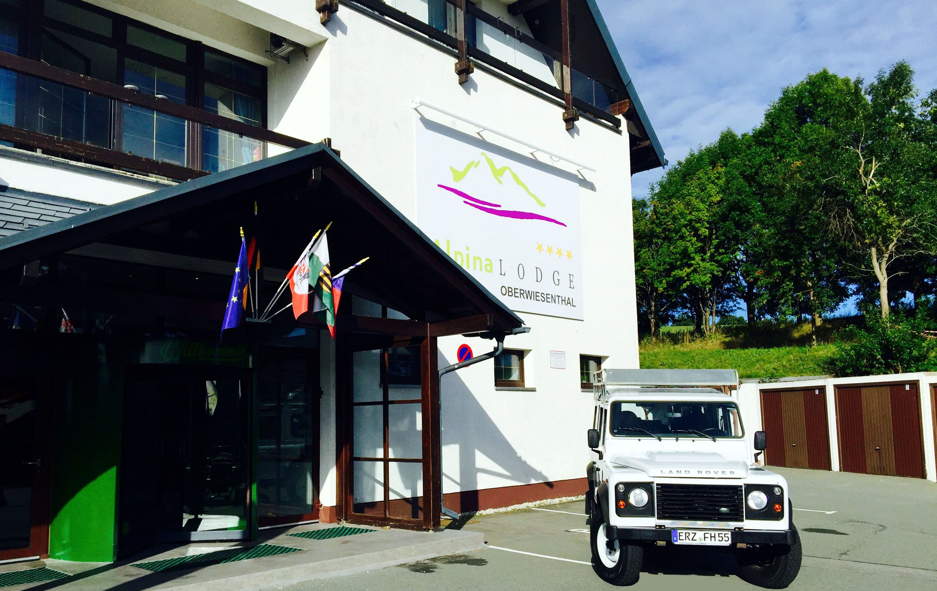 Ein Gebäude mit einem Schild, auf dem „Alpina Lodge Oberwiesenthal“ steht, und ein weißer Land Rover davor geparkt.