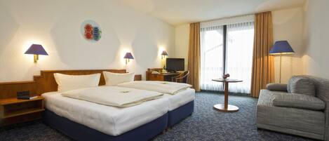 A hotel room with a double bed, a sofa, a desk with a TV, and two lamps.