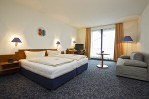 A hotel room with a double bed, a sofa, a desk with a TV, and two lamps. - Alpina Lodge Hotel Oberwiesenthal (Oberwiesenthal)