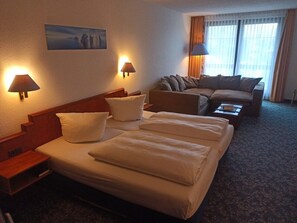 A hotel room with a bed, a sofa, two wall-mounted lamps, a painting, and a window with curtains. - Alpina Lodge Hotel Oberwiesenthal (Oberwiesenthal)