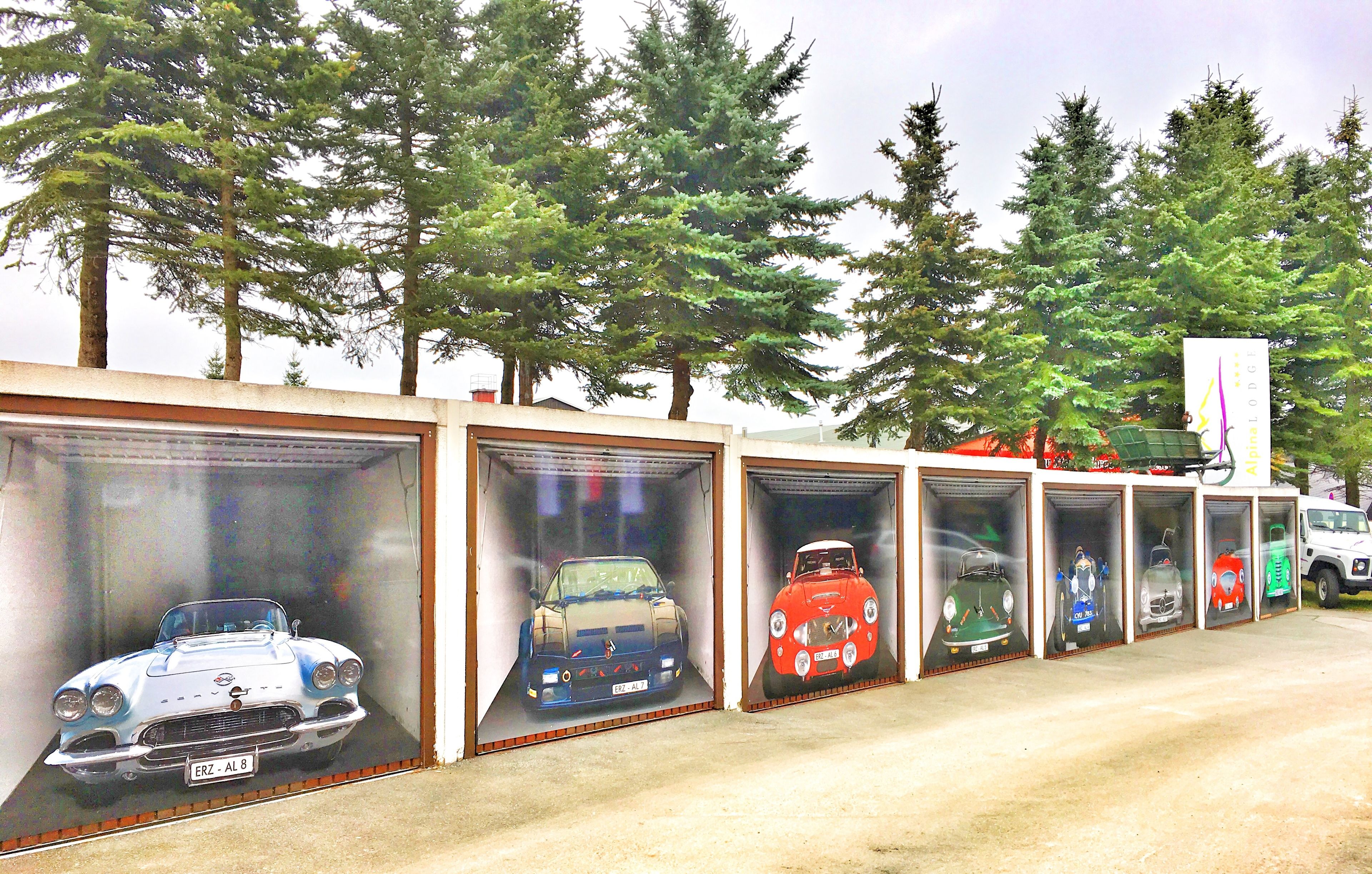 A row of garage doors with various classic cars displayed inside.