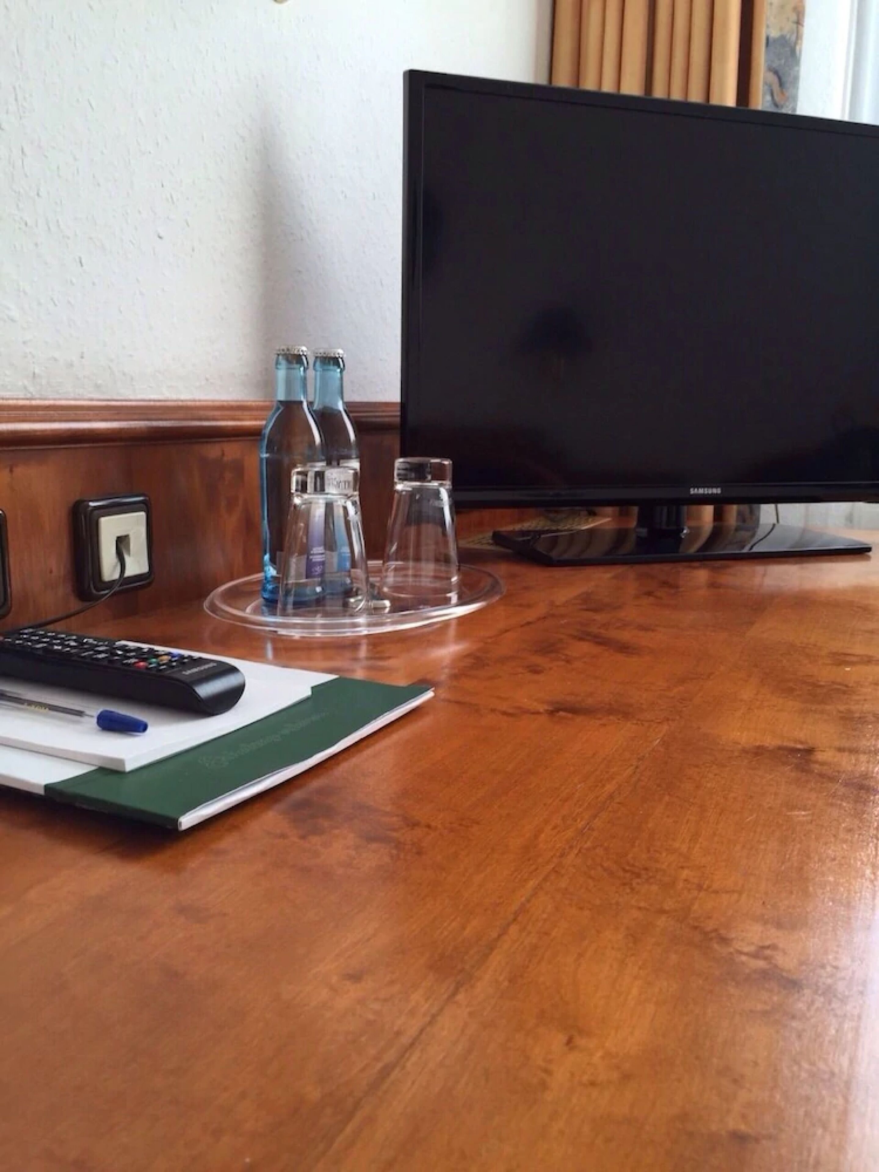 Una scrivania in legno con un telecomando, un quaderno e due bottiglie trasparenti.