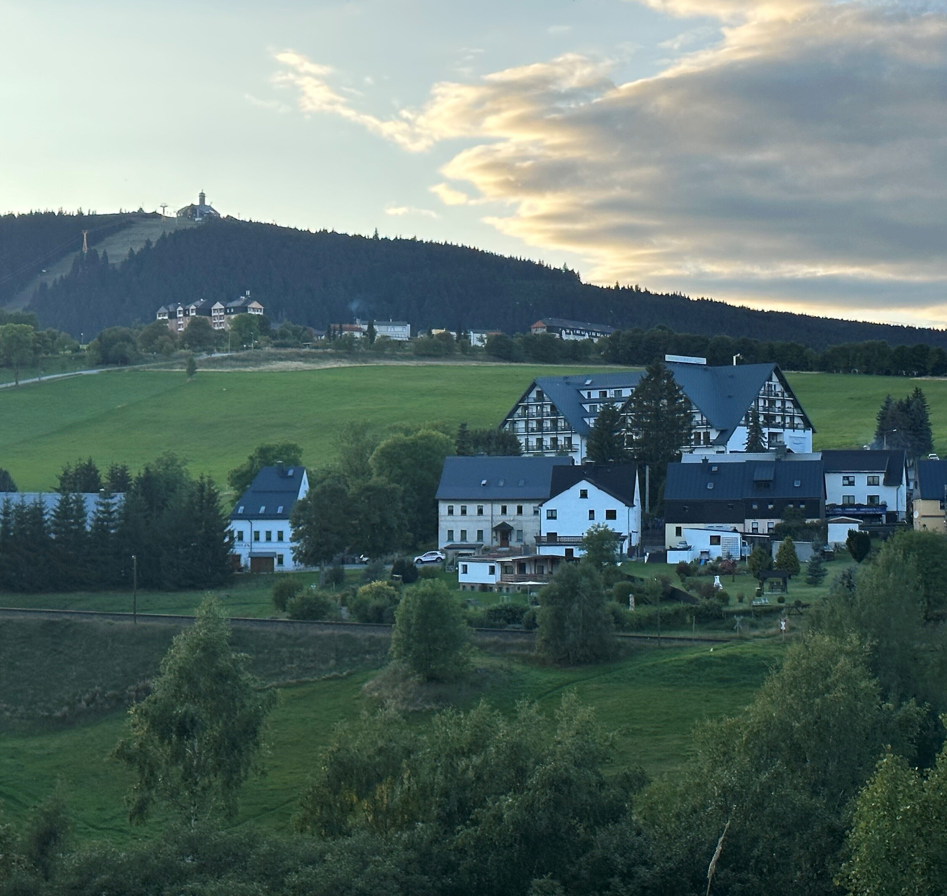 A rural village with traditional houses, a church, and a hill with a tower.