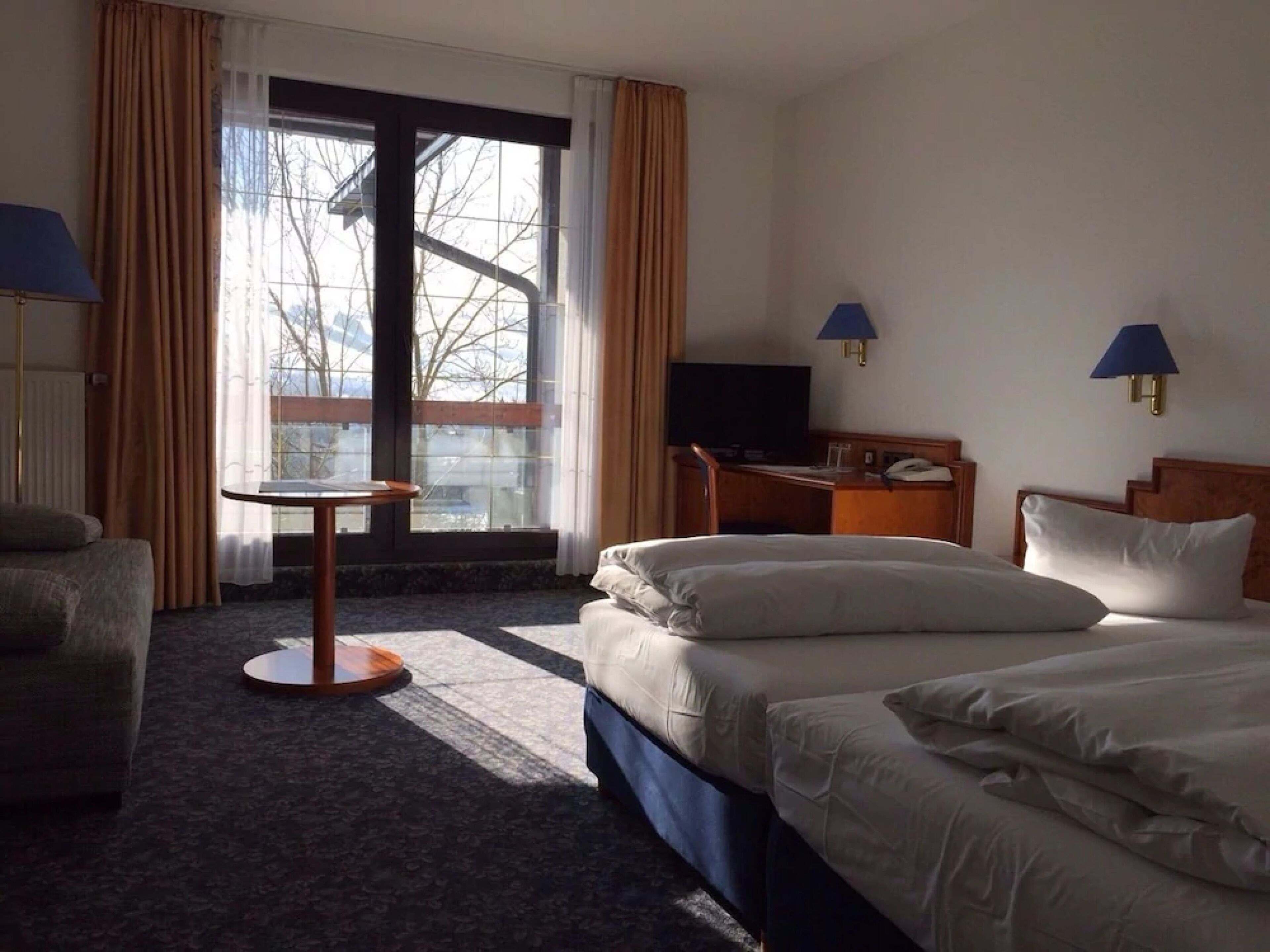A hotel room with two beds, a desk, a chair, and a window with curtains.
