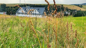 A large building with a sloped roof, surrounded by a grassy field and a wind turbine in the background.