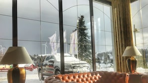 A room with a large window, leather sofa, two lamps, and a view of a snowy landscape with a vehicle outside.