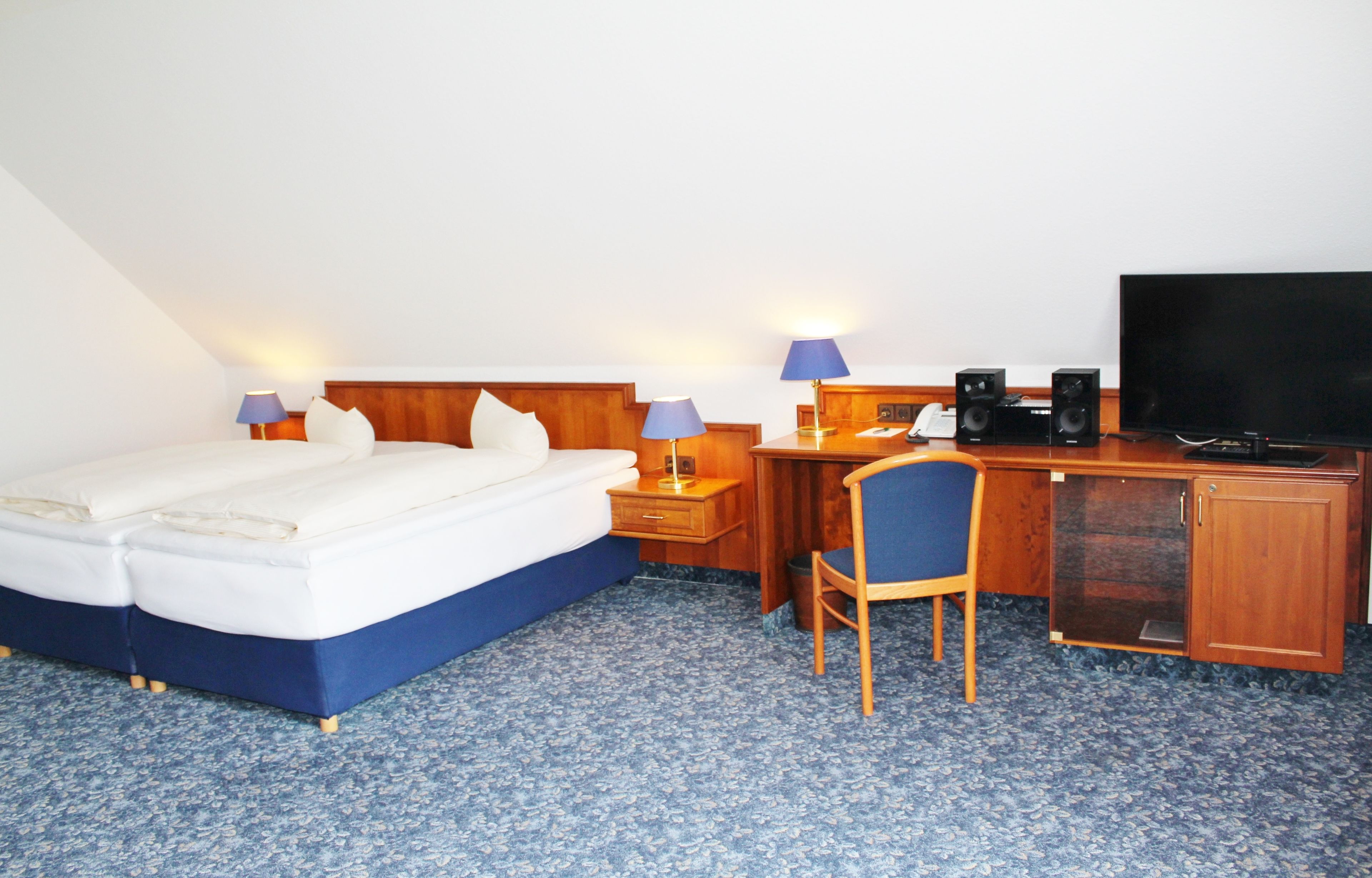 Habitación de hotel con cama, escritorio, silla, televisor y altavoces.