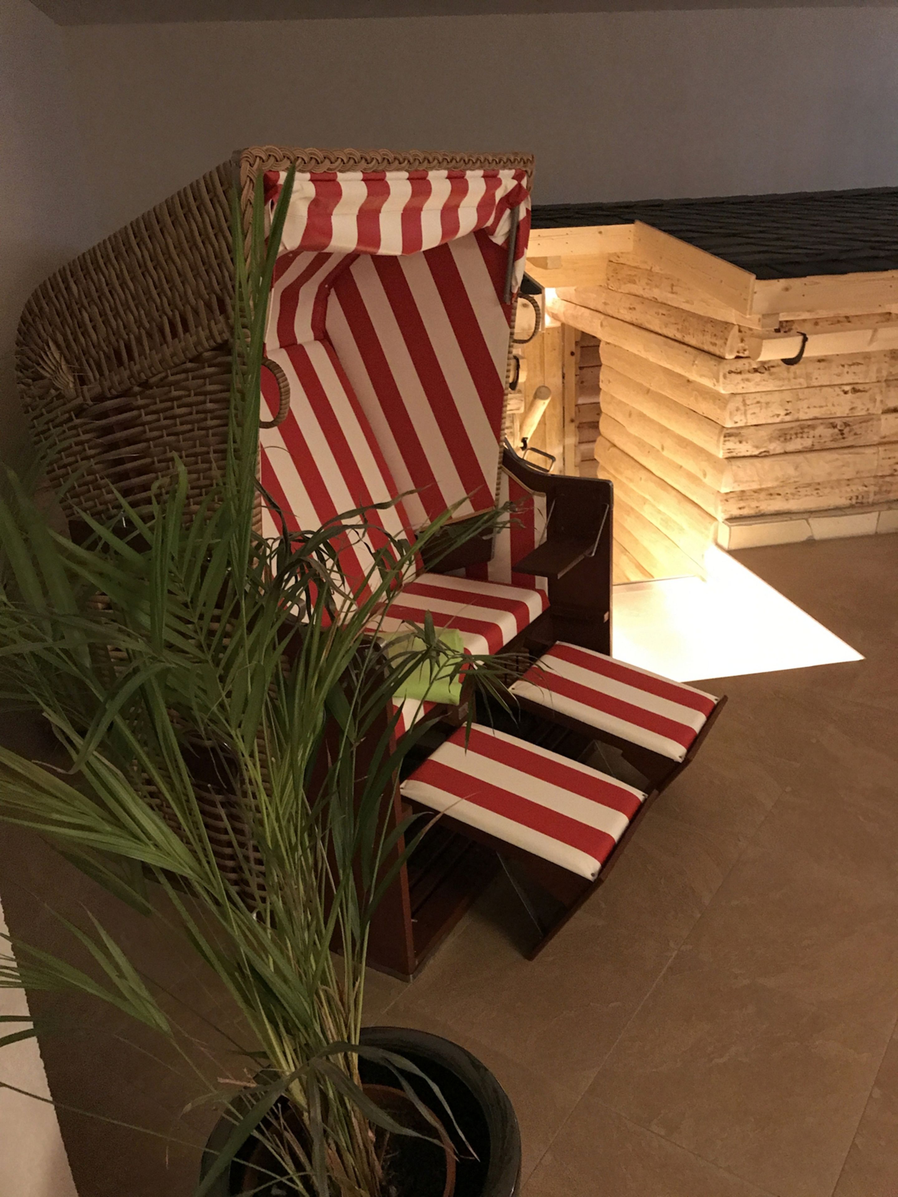 A wicker lounge chair with red and white striped cushions, a potted plant, and a stack of wooden planks in the background.
