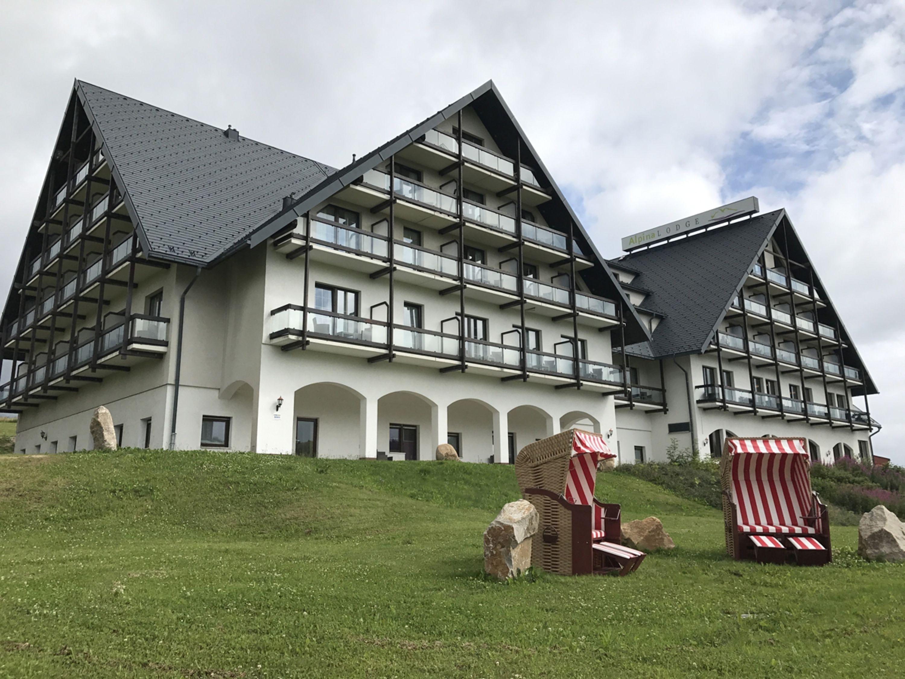 Ein mehrstöckiges Hotel mit Balkonen, einer Rasenfläche und zwei Liegestühlen.