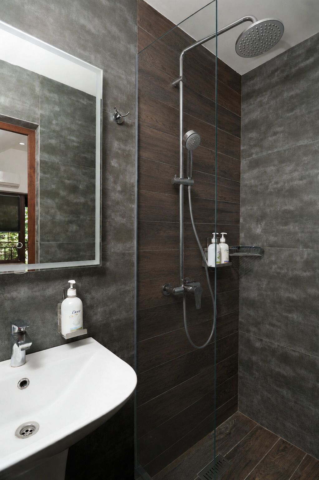 Un baño moderno con ducha envuelta en vidrio, lavamanos blanco y un espejo grande.
