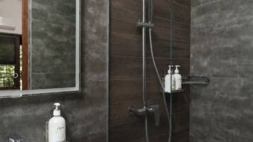Un baño moderno con ducha envuelta en vidrio, lavamanos blanco y un espejo grande.