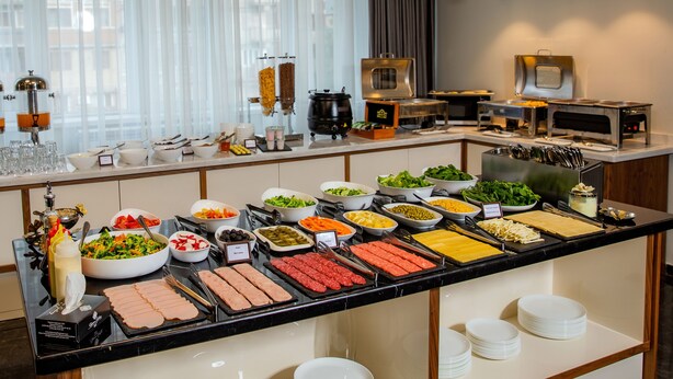 En buffet med forskellige retter og bestik, herunder salatskåle, fade med kød samt en kaffestation.