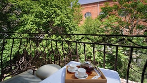 Un balcón con una mesa lista para el té, rodeado de abundante follaje y un edificio de ladrillo al fondo.