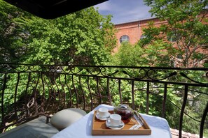 A balcony with a table set for tea, surrounded by lush greenery and a brick building in the background. - Elysium Gallery Hotel (Yerevan)