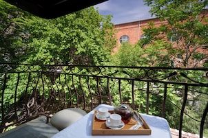 Een balkon met een gedekte tafel voor thee, omringd door weelderige begroeiing en een bakstenen gebouw op de achtergrond.