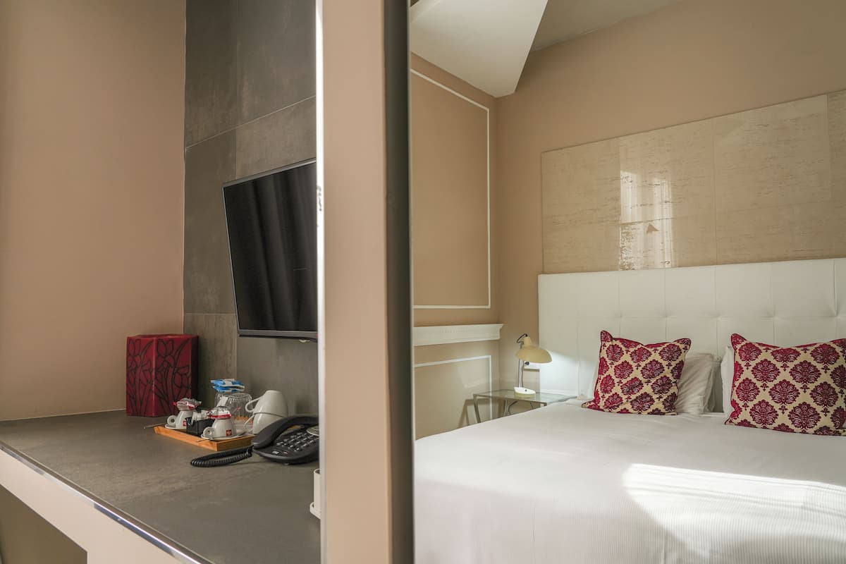 A hotel room with a bed, bedside table, lamp, and a red box.