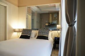 Contemporary hotel room with a large bed, bedside table, and bathroom featuring a shower and sink.