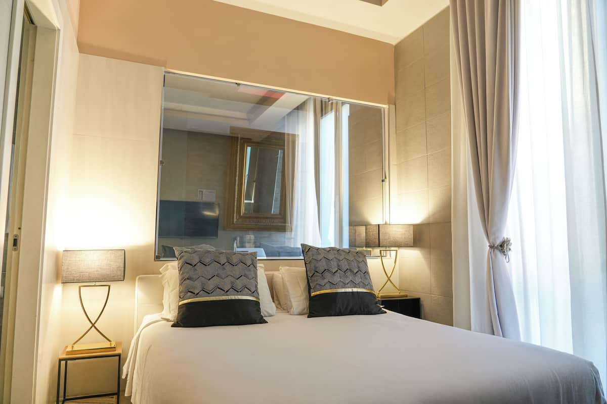 A hotel room with a large bed, two bedside tables with lamps, a large mirror, and a window with curtains.