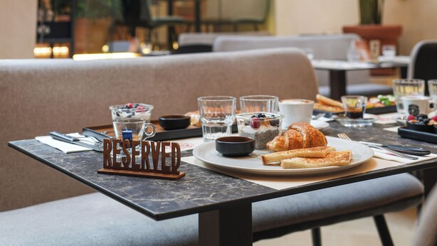 A dining area with a table set for breakfast, including croissants and coffee, in a modern building with a high ceiling and large windows. - Corso Boutique Luxury Rooms (Rome)