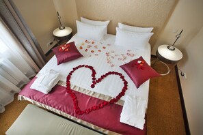 A hotel room with a neatly made bed, a heart-shaped arrangement of rose petals, and a red and white color scheme.