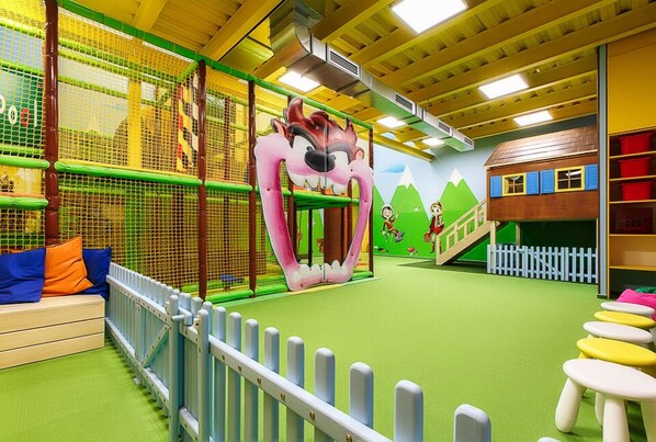Zona de juegos infantiles con una gran estructura de oso rosa, una red de escalada y una casita.