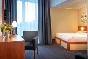 A hotel room with a bed, a desk with a lamp, a chair, and a vase of flowers. - Atrium Hotel (Vysoké Tatry)