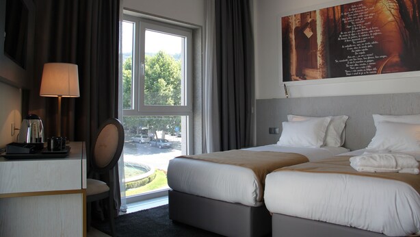 A hotel room with two beds, a desk with a lamp, and a large window with curtains. - Hotel José Régio (Portalegre)