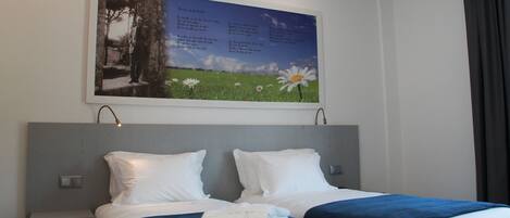 A hotel room with two beds, a nightstand, a wall-mounted artwork, and a window with curtains.