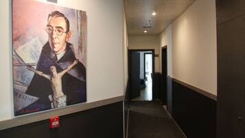 Un corridoio con un quadro grande sulla parete sinistra, un rilevatore di fumo a pavimento e una porta in fondo.