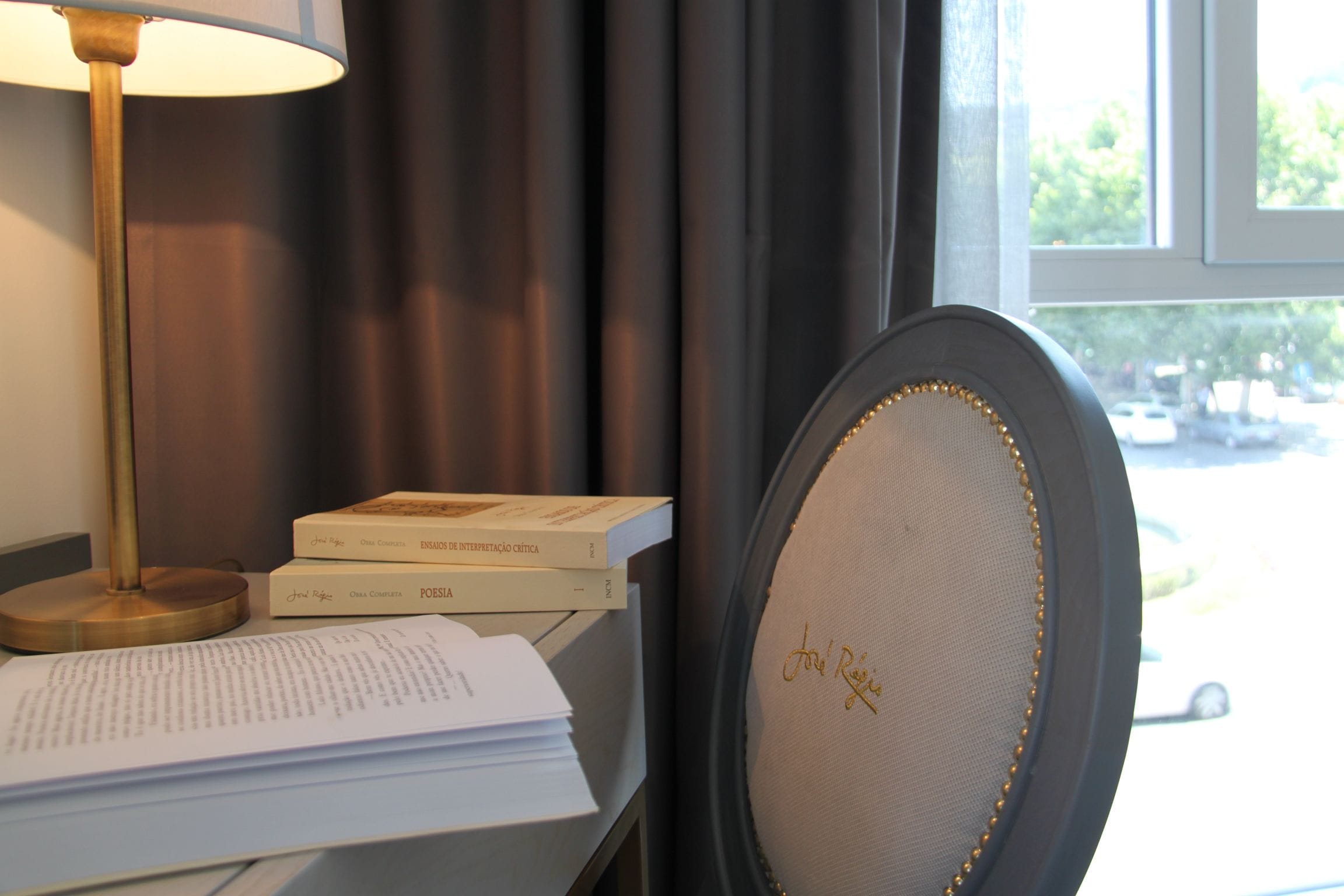 Ein Schreibtisch mit Büchern, einer Lampe und einem Stuhl mit Unterschrift auf der Rückenlehne.