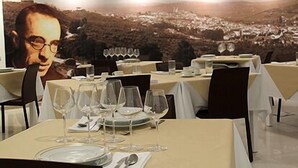 A restaurant with tables set for dining, a large poster on the wall, and a view of a town in the background. - Hotel José Régio (Portalegre)