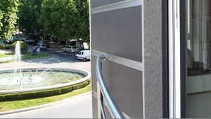 A hotel room with a bed, a small table, and a view of a fountain and parked cars outside. - Hotel José Régio (Portalegre)