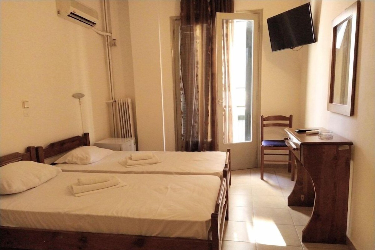 Une chambre avec deux lits, un bureau, une chaise, une télévision et une fenêtre avec des rideaux.
