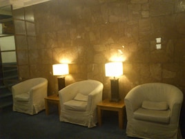 Una habitación con tres sillas y dos lámparas frente a una pared de piedra.