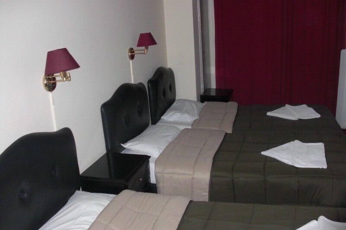 Una habitación de hotel con dos camas, cada una con cabecera y mesita de noche. Hay dos lámparas en la pared.