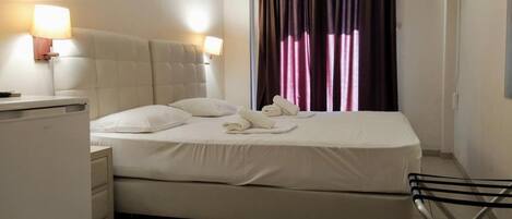 Una habitación de hotel con cama, lámparas de noche, televisión y ventana con cortinas.