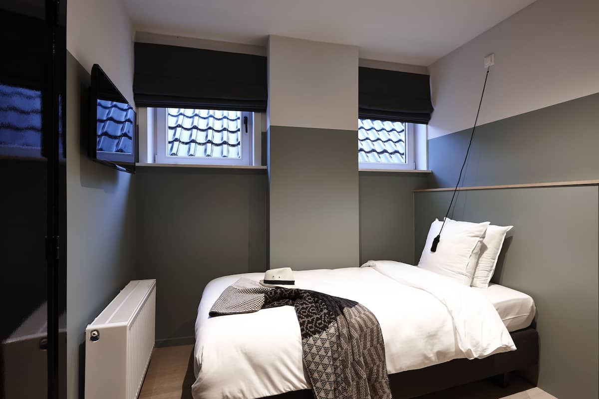 A bedroom with a bed, a radiator, and a television mounted on the wall.