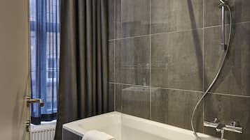 Une salle de bain moderne avec une douche à parois de verre, une baignoire blanche et des murs recouverts de carreaux foncés.
