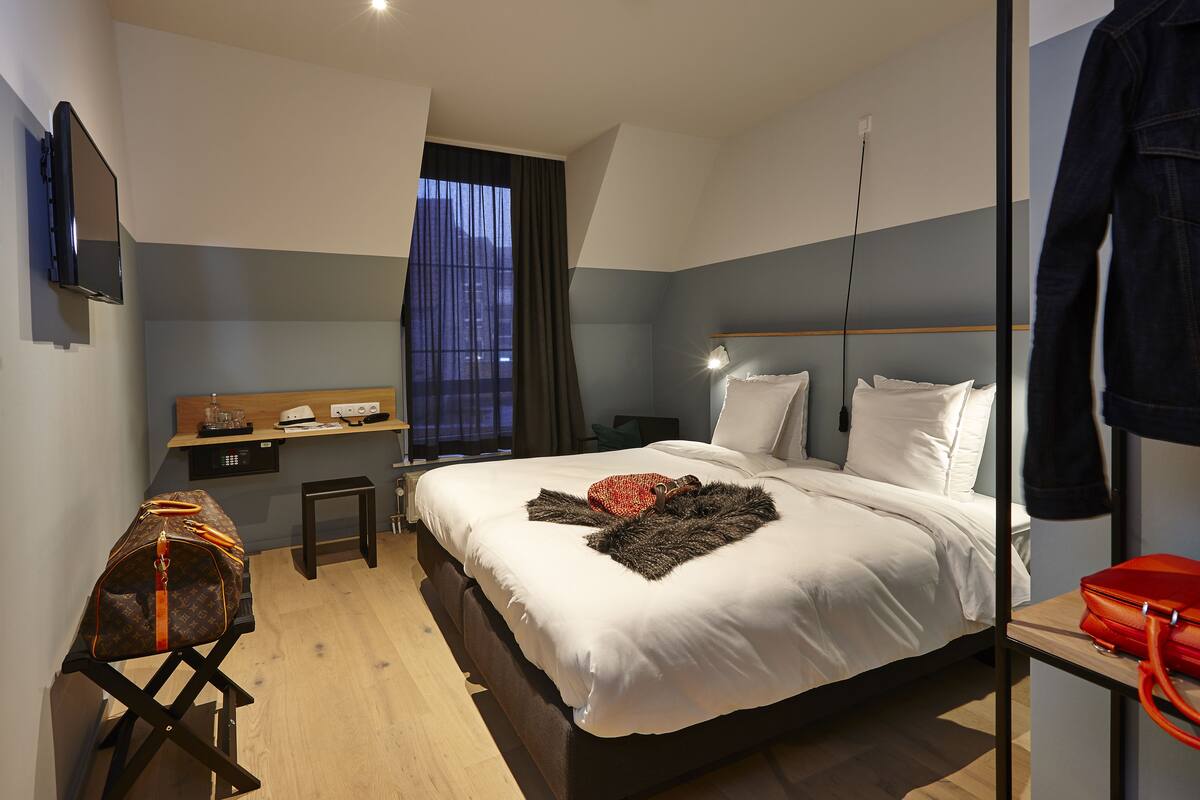 A modern hotel room with a bed, bedside table, and a desk with a computer.