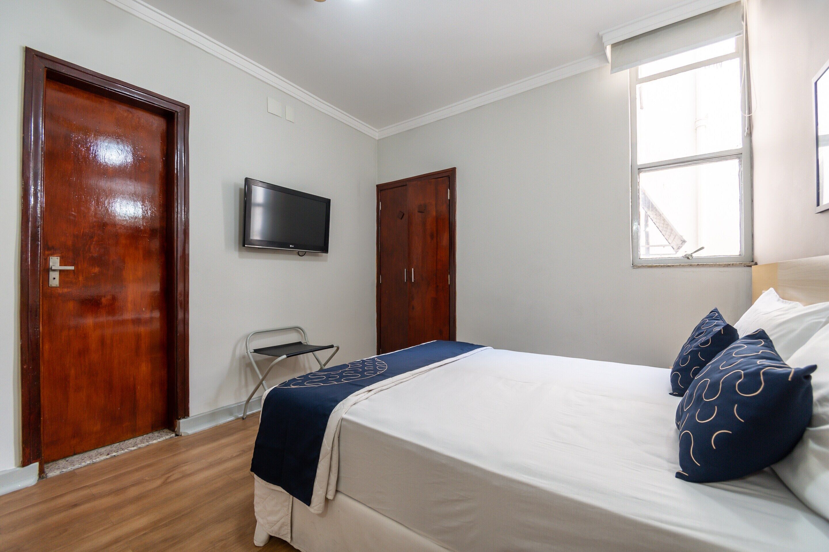 A bedroom with a bed, a television, two doors, and a window.