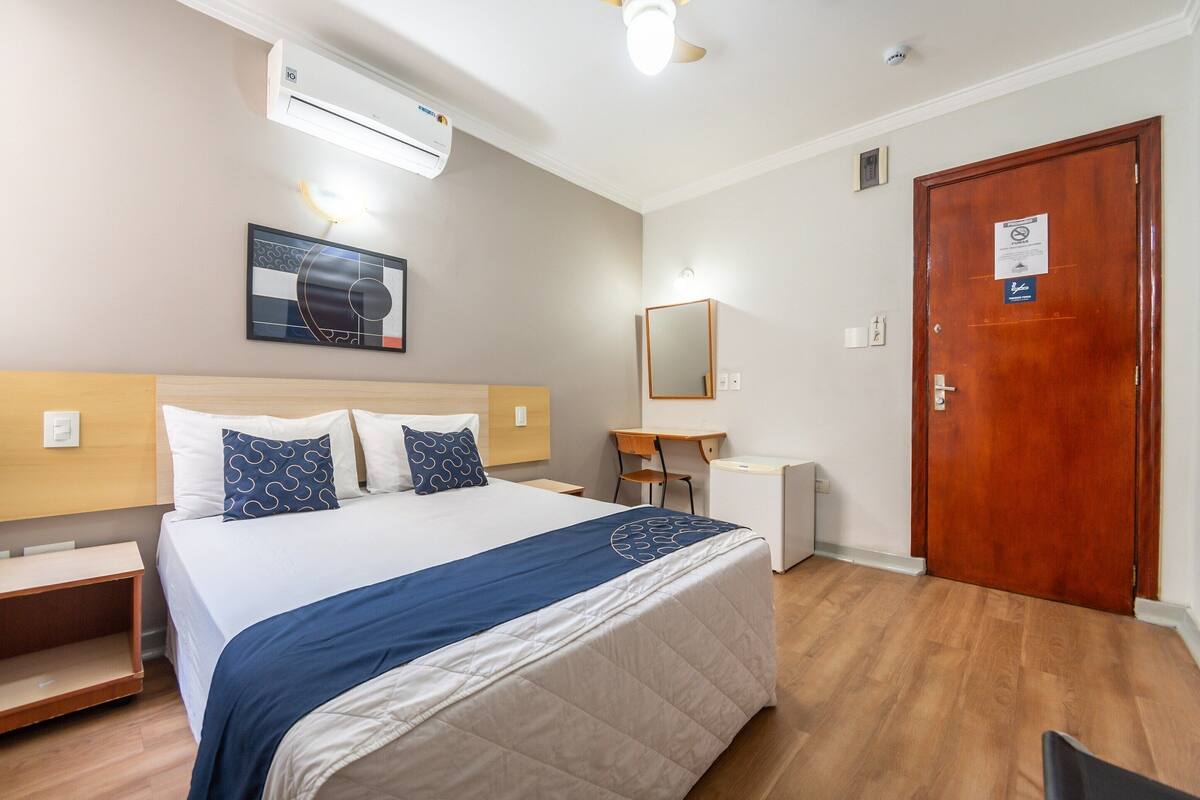 A hotel room with a bed, bedside table, desk, chair, and a door.