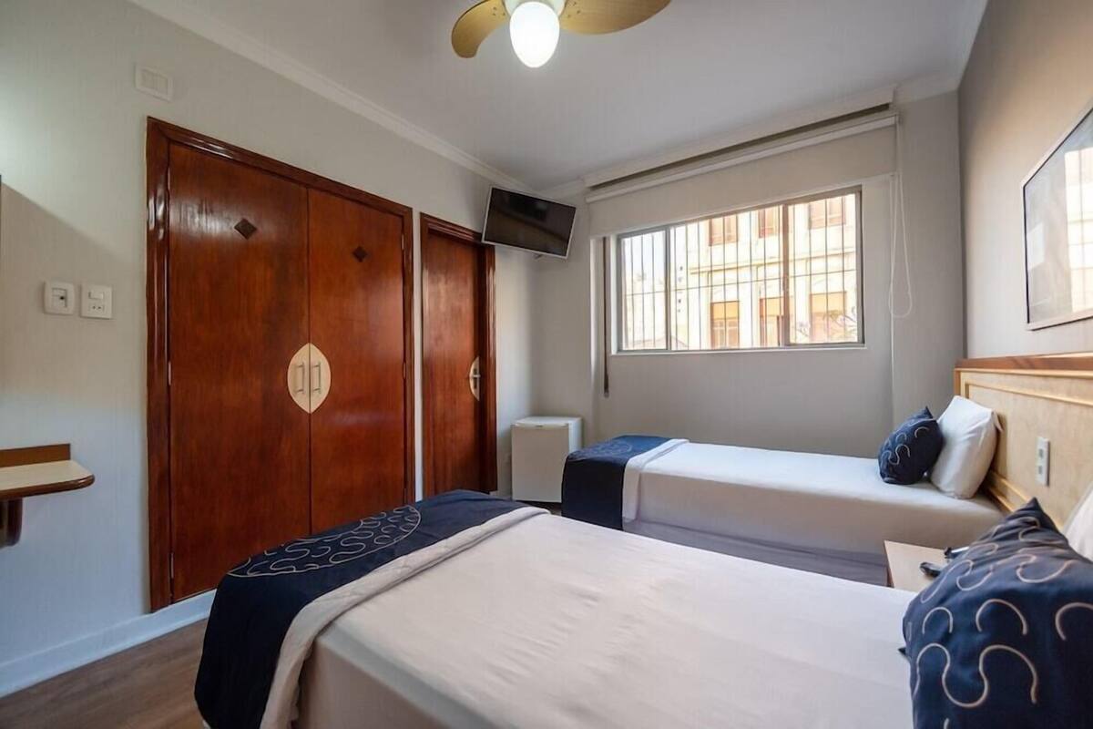A hotel room with two beds, a TV, a window, and a wardrobe.