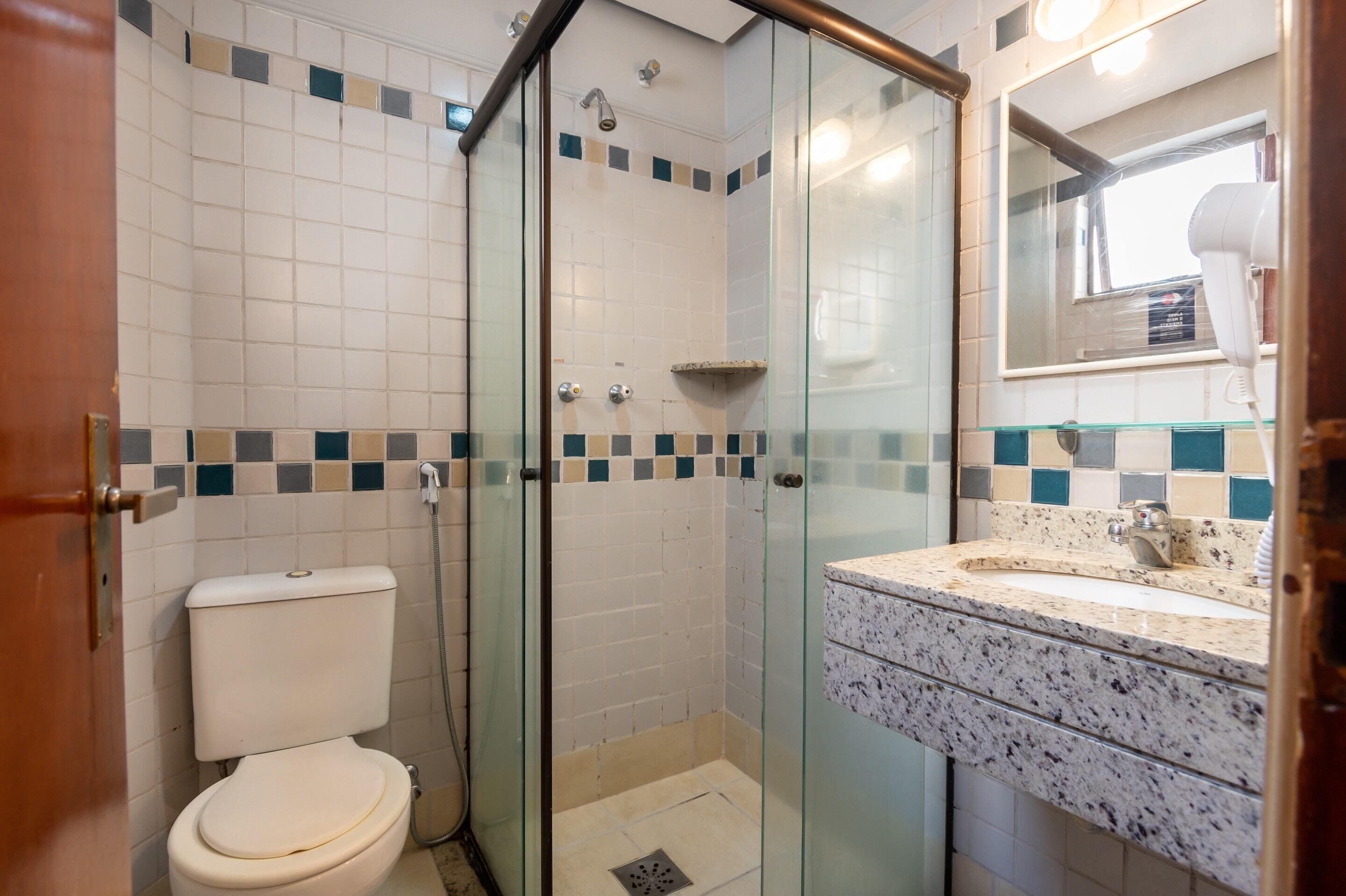 A bathroom with a glass-enclosed shower, a toilet, and a sink with a mirror above it.