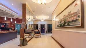 A hotel lobby with a reception desk, seating area, and a large framed cityscape painting. - Rede Andrade Piratininga (São Paulo)