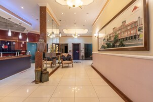 Una hall d'albergo con reception, angolo relax e un grande quadro che raffigura un panorama cittadino.
