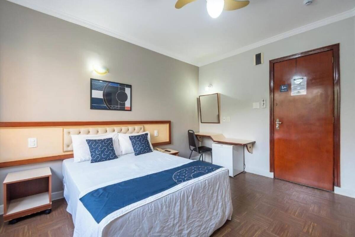 A hotel room with a bed, desk, chair, and a door.