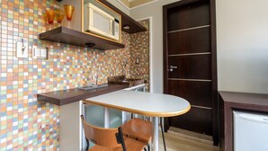 A compact kitchen with a tiled backsplash, a microwave, and a small dining area with a chair. - Rede Andrade Piratininga (São Paulo)