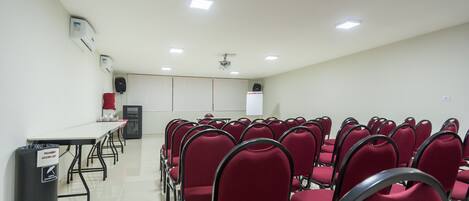 A conference room with rows of red chairs, a white table, and a projector screen.
