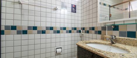 A bathroom with white tiles, a toilet, a sink with a granite countertop, and a mirror.