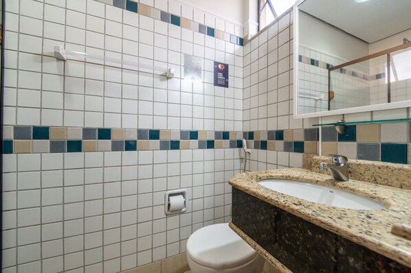 Un baño con azulejos blancos, un inodoro, un lavabo con encimera de granito y un espejo.